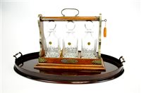 Lot 135 - An Edwardian mahogany butlers tray with an oak tantalus accommodating a trio of crystal decanters.