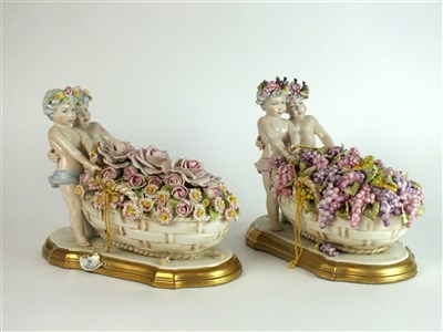 Lot 321 - A pair of Capodimonte porcelain figures of cherubs pulling baskets of flowers and fruit