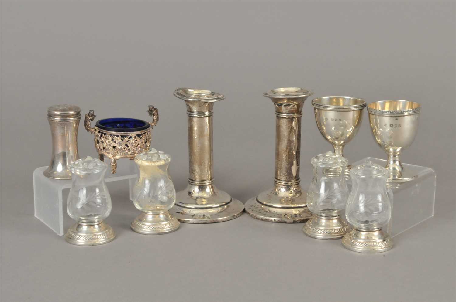 Lot 3 - A pair of short silver candlesticks, together with two silver egg cups, a salt with blue glass liner, a pepperette and white metal mounted glass salt/pepper pots