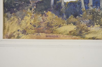 Lot 175 - George Robert Rushton (1869-1947) Lady walking amongst trees with a lakeside village beyond