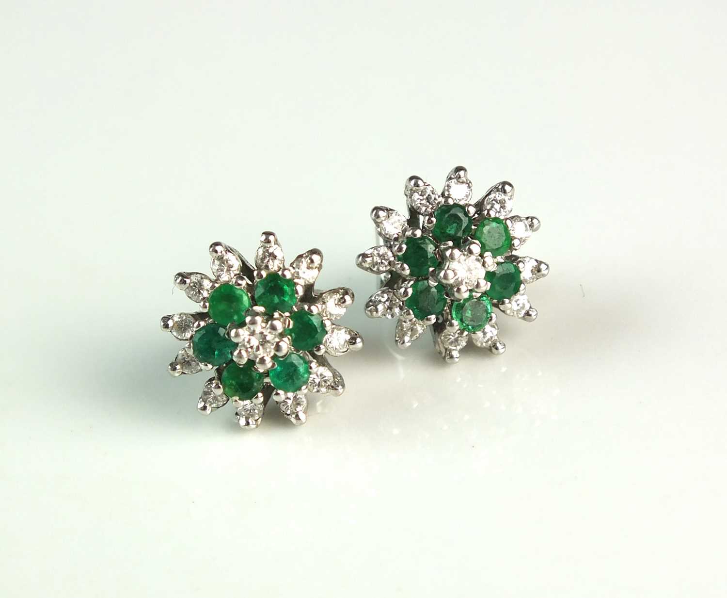 Lot 86 - A pair of 18ct white gold emerald and diamond cluster earrings