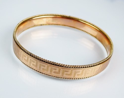 Lot 184 - A 9ct gold slave bangle, with stylised Greek...